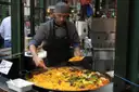 A cook serving paella from a giant pan at a London market stall