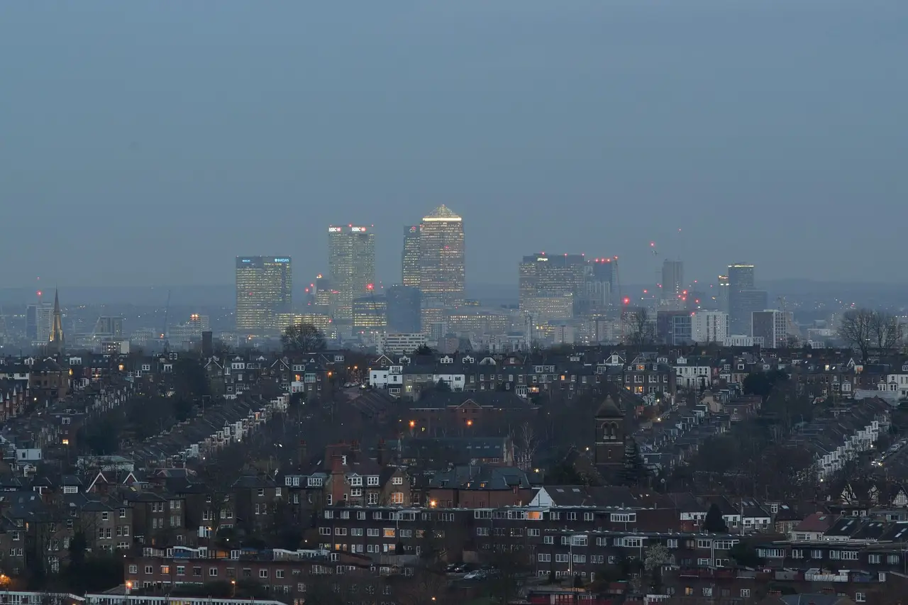 Rows of terraced houses stretching toward the towers of Canary Wharf at dusk, seen from Alexandra Palace in London