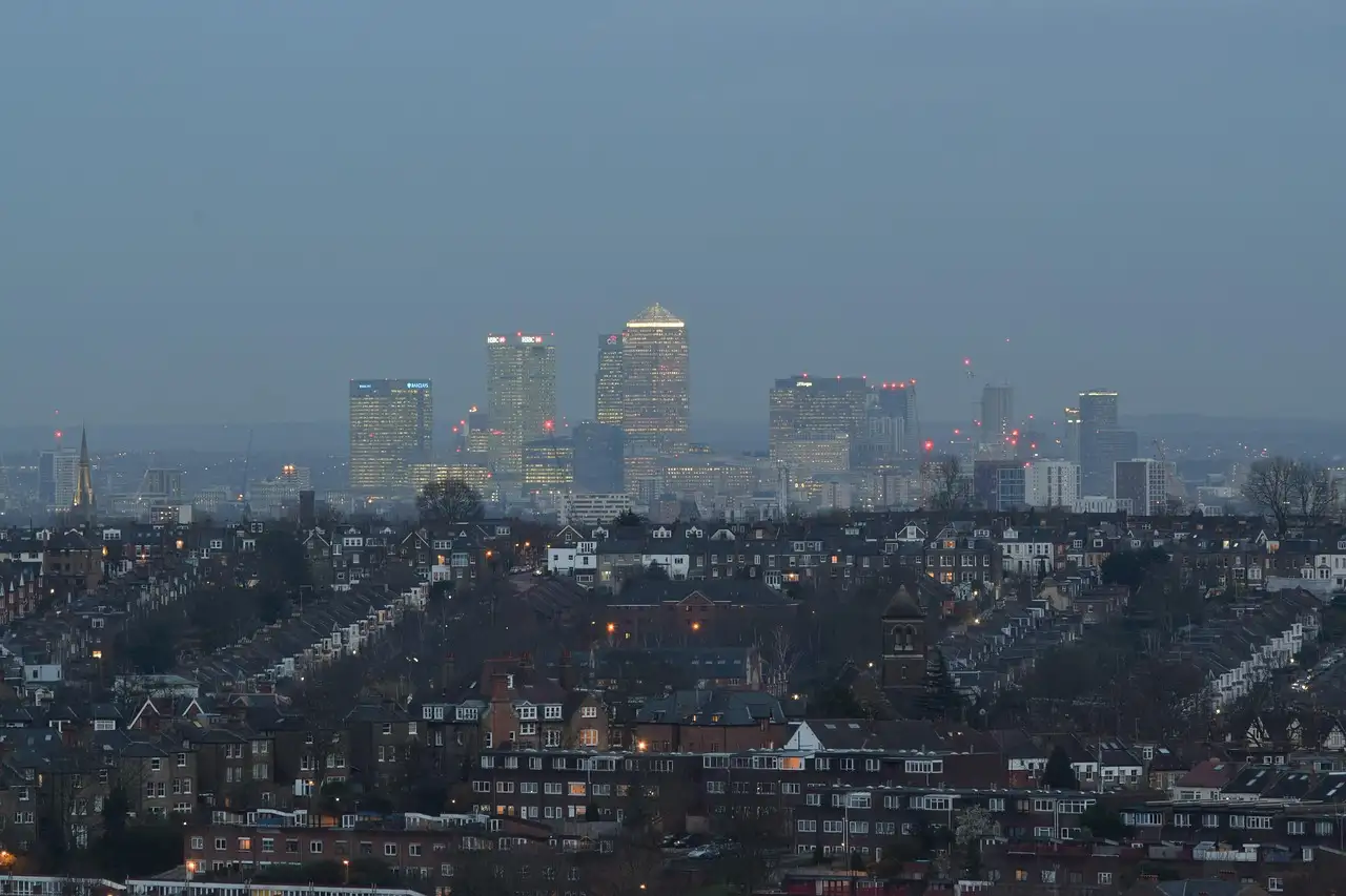 Rows of terraced houses stretching toward the towers of Canary Wharf at dusk, seen from Alexandra Palace in London