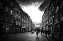 A narrow London street of brick terraces in black and white under a stormy sky