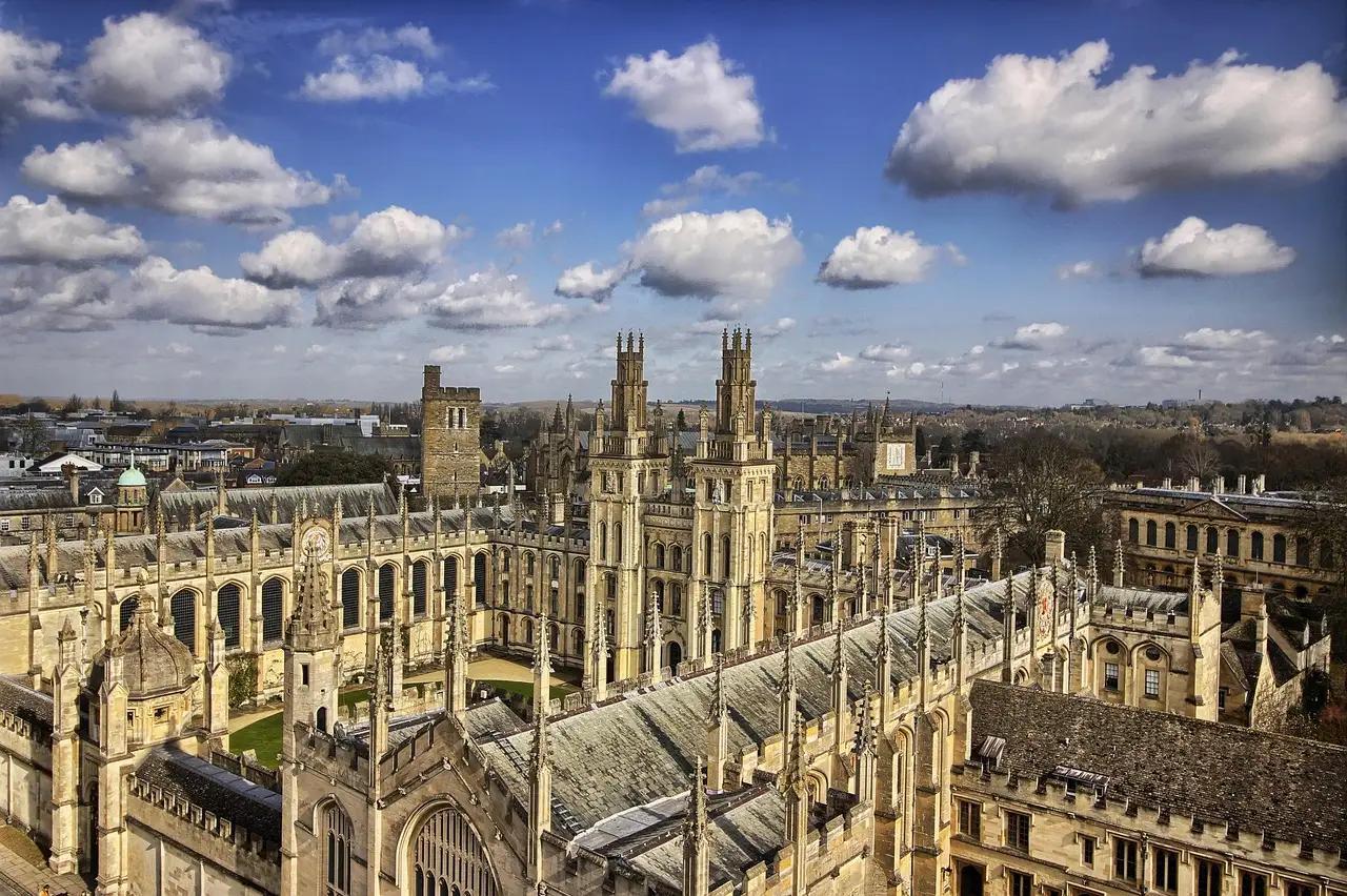 The honey-coloured Gothic towers and rooftops of Oxford's colleges seen from above under a blue sky with clouds