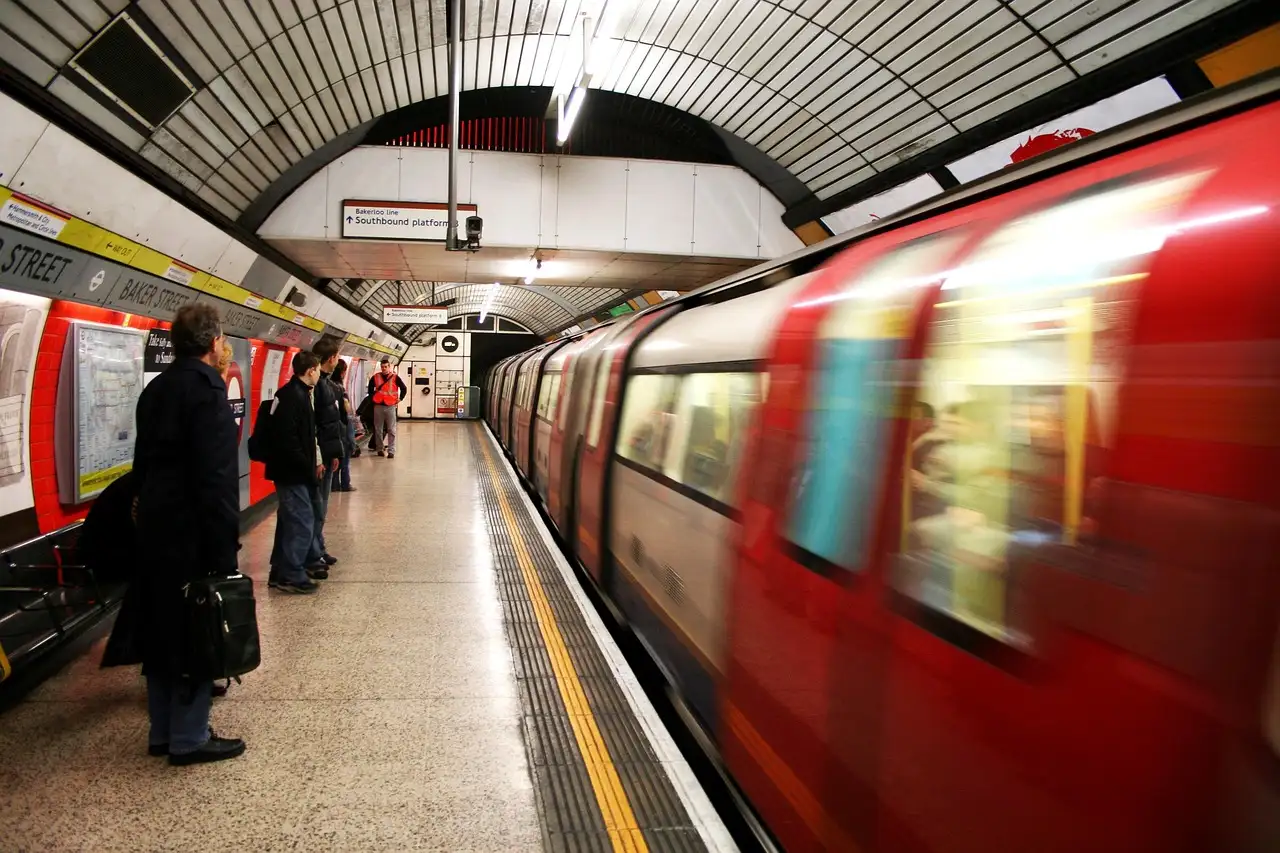A London Underground train pulling into a curved platform as passengers wait