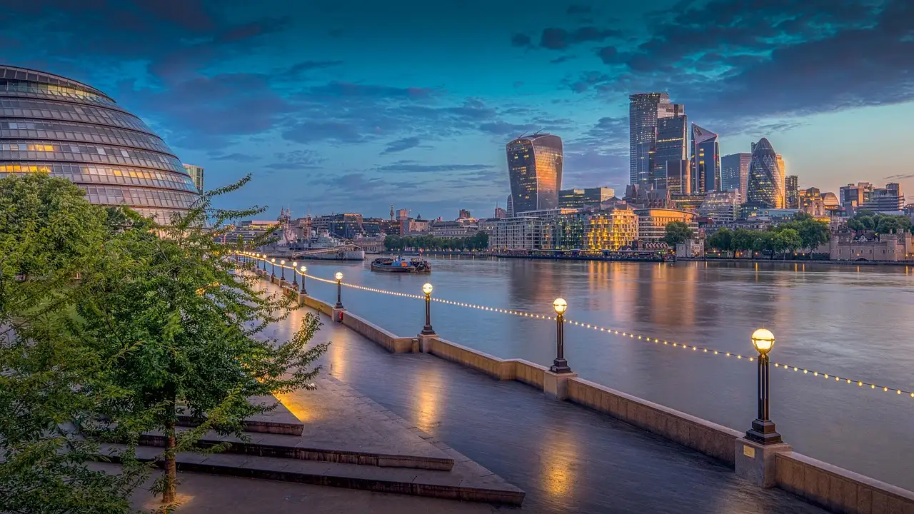 The London skyline at dusk seen from a riverside walk on the Thames, towers glowing in the distance