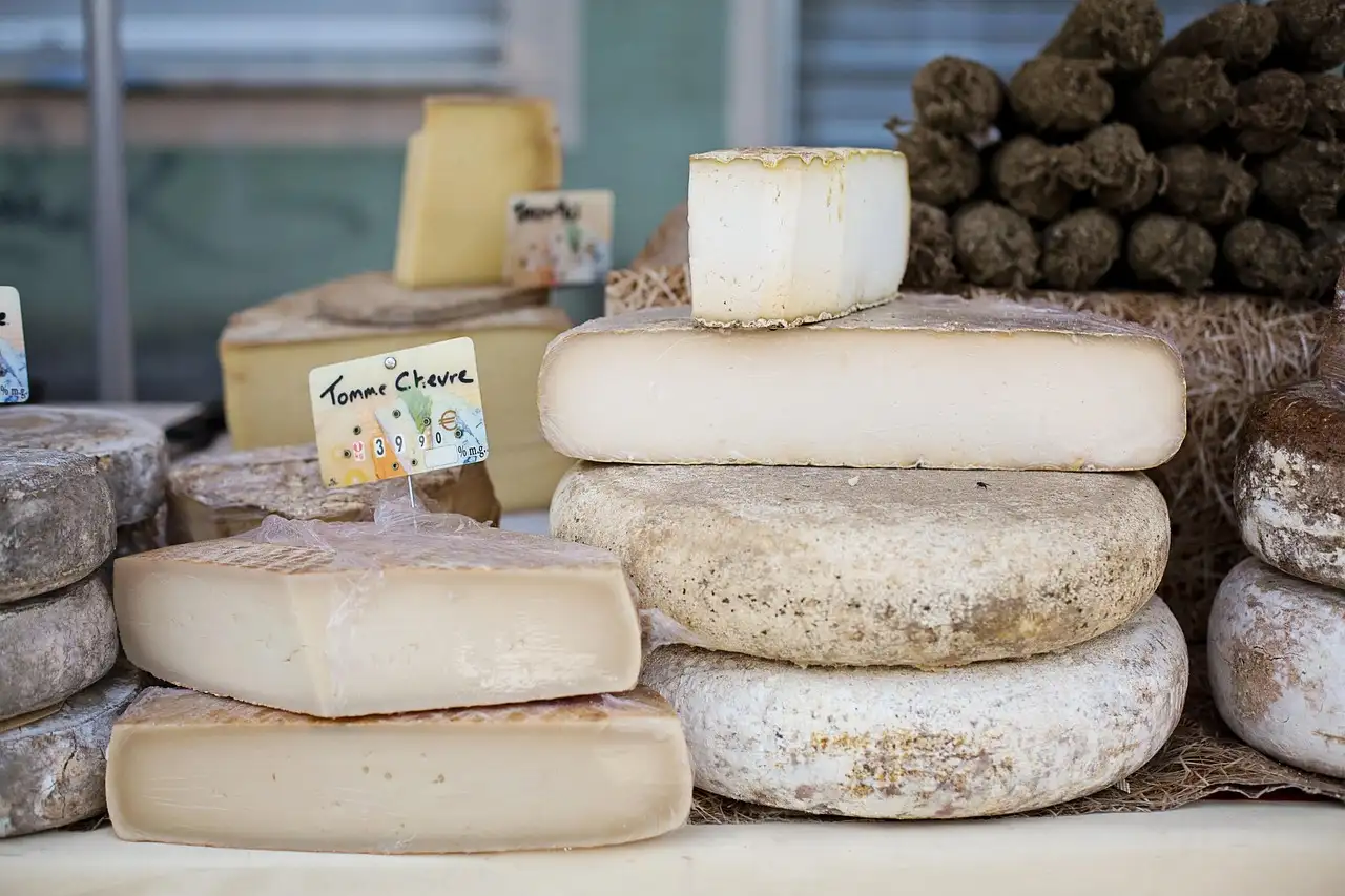 Whole and cut cheeses stacked on a market stall