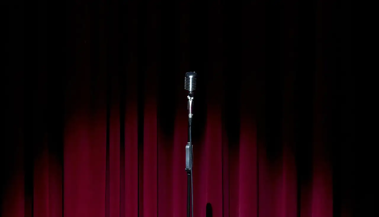 A single microphone on a stand in front of a red stage curtain
