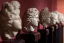 A row of carved marble heads against a dark red museum wall