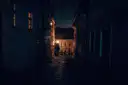 A narrow cobbled alley at night with one lamp lit at the end