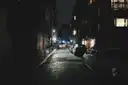 A narrow terraced street at night with a few lit windows
