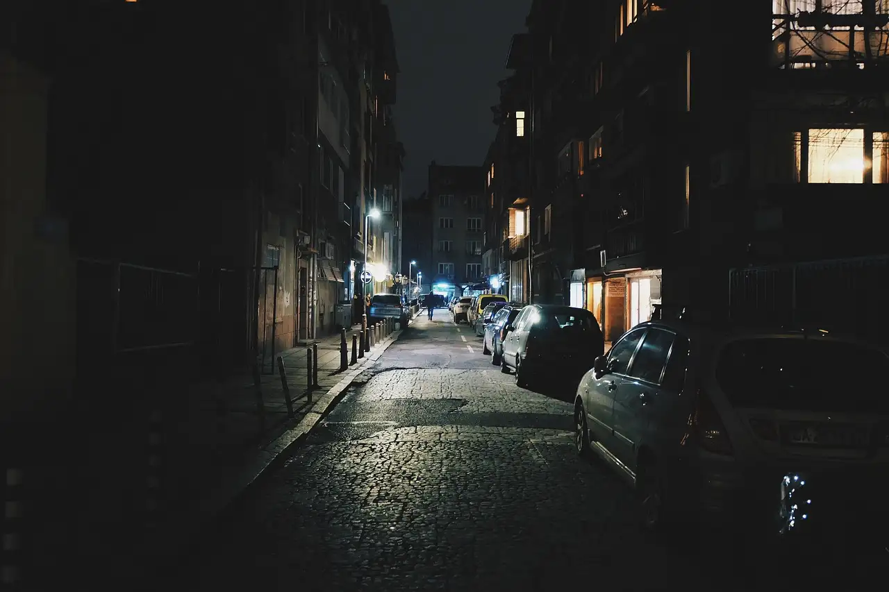 A narrow terraced street at night with a few lit windows