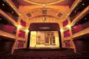 An ornate gilded theatre with red boxes and a lit stage