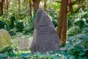 A rough memorial stone among ivy-covered graves in an overgrown cemetery
