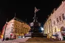 Piccadilly Circus at night, with the Eros statue lit in front of curved stone buildings