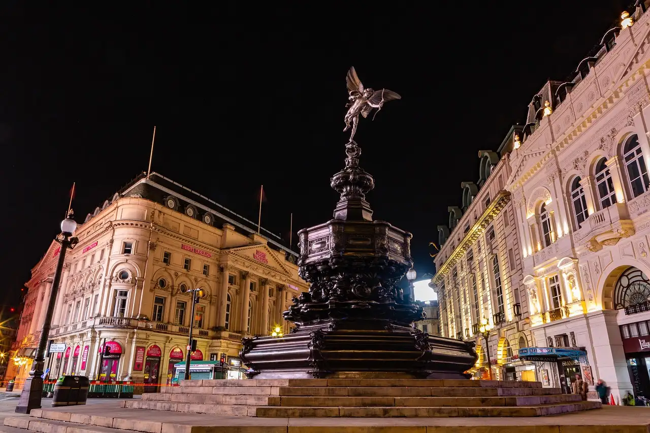 Piccadilly Circus at night, with the Eros statue lit in front of curved stone buildings