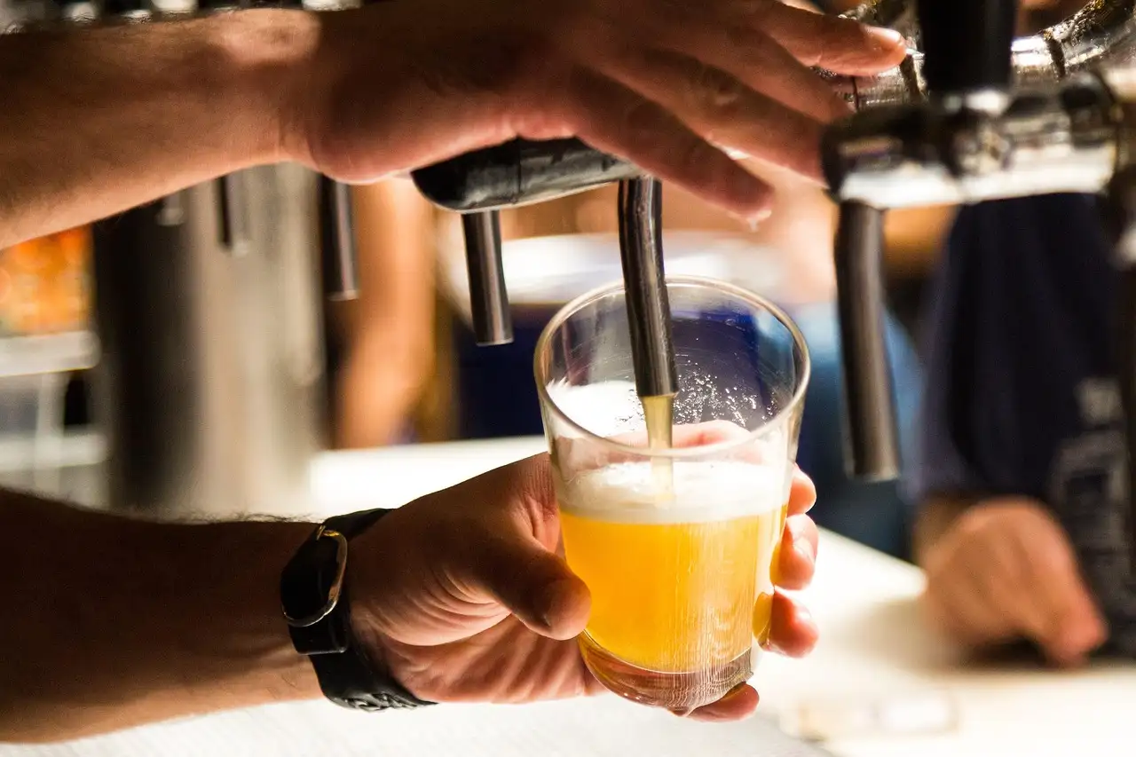 A hand pouring a pale beer from a bar tap