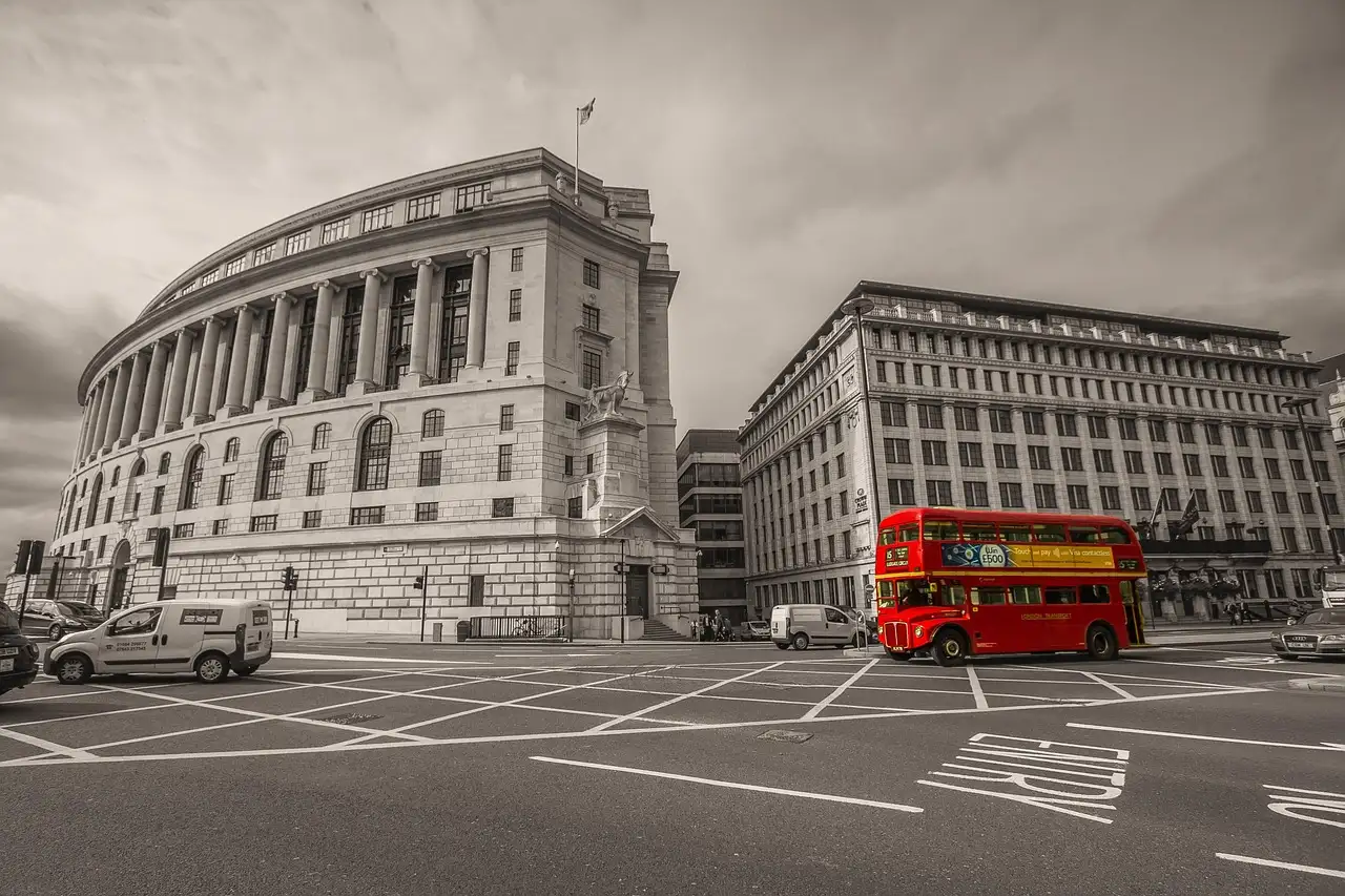 A red double-decker bus at a London junction, picked out in colour against black and white