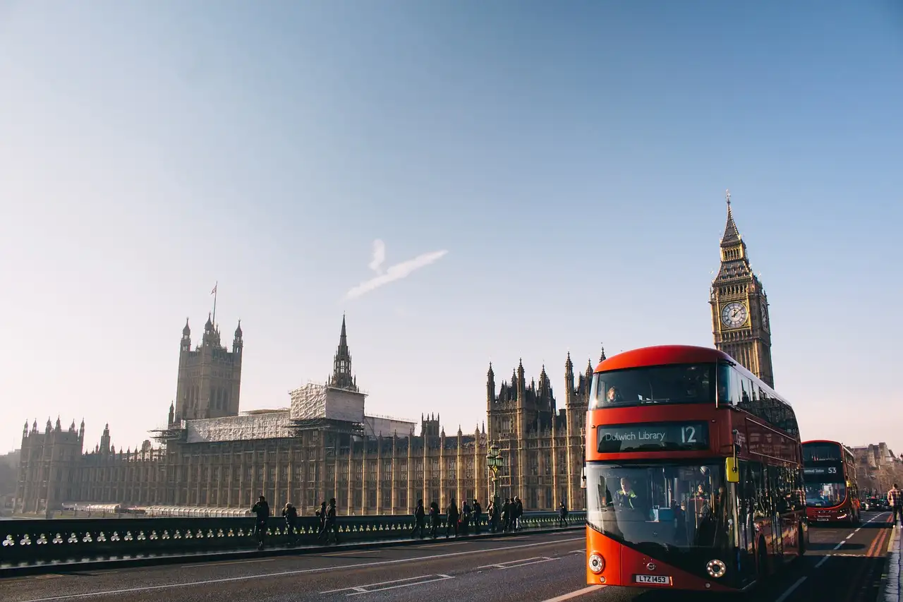 A red double-decker bus on Westminster Bridge in front of the Houses of Parliament and Big Ben