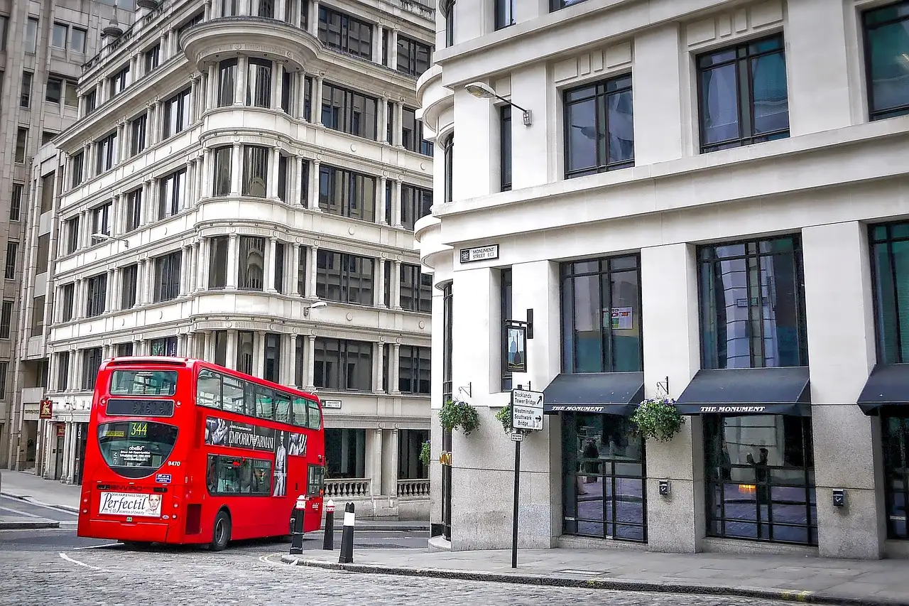 A red double-decker bus turning a corner between London office buildings