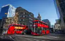 Two red double-decker buses passing office buildings in the City of London