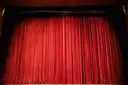 A closed red velvet stage curtain under stage lights