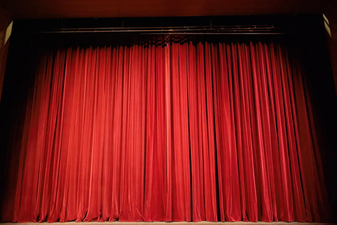 A closed red velvet stage curtain under stage lights