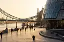 People walking along the Thames riverside path towards Tower Bridge in golden morning light