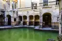 Stone arches and steps around the green water of the Roman Baths