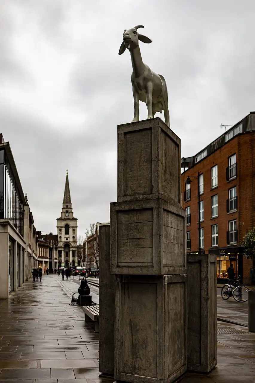 The spire of Christ Church Spitalfields at the end of a wet East End street, past a goat statue on stone crates