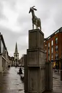 The spire of Christ Church Spitalfields at the end of a wet East End street, past a goat statue on stone crates