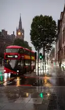 A red double-decker bus on a wet street by St Pancras, next to King's Cross, the station clock tower behind