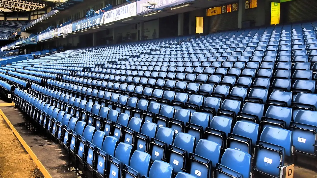 Rows of empty blue seats at Stamford Bridge, seen from pitch side