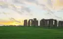 Stonehenge on the grassy plain at sunset under a golden sky