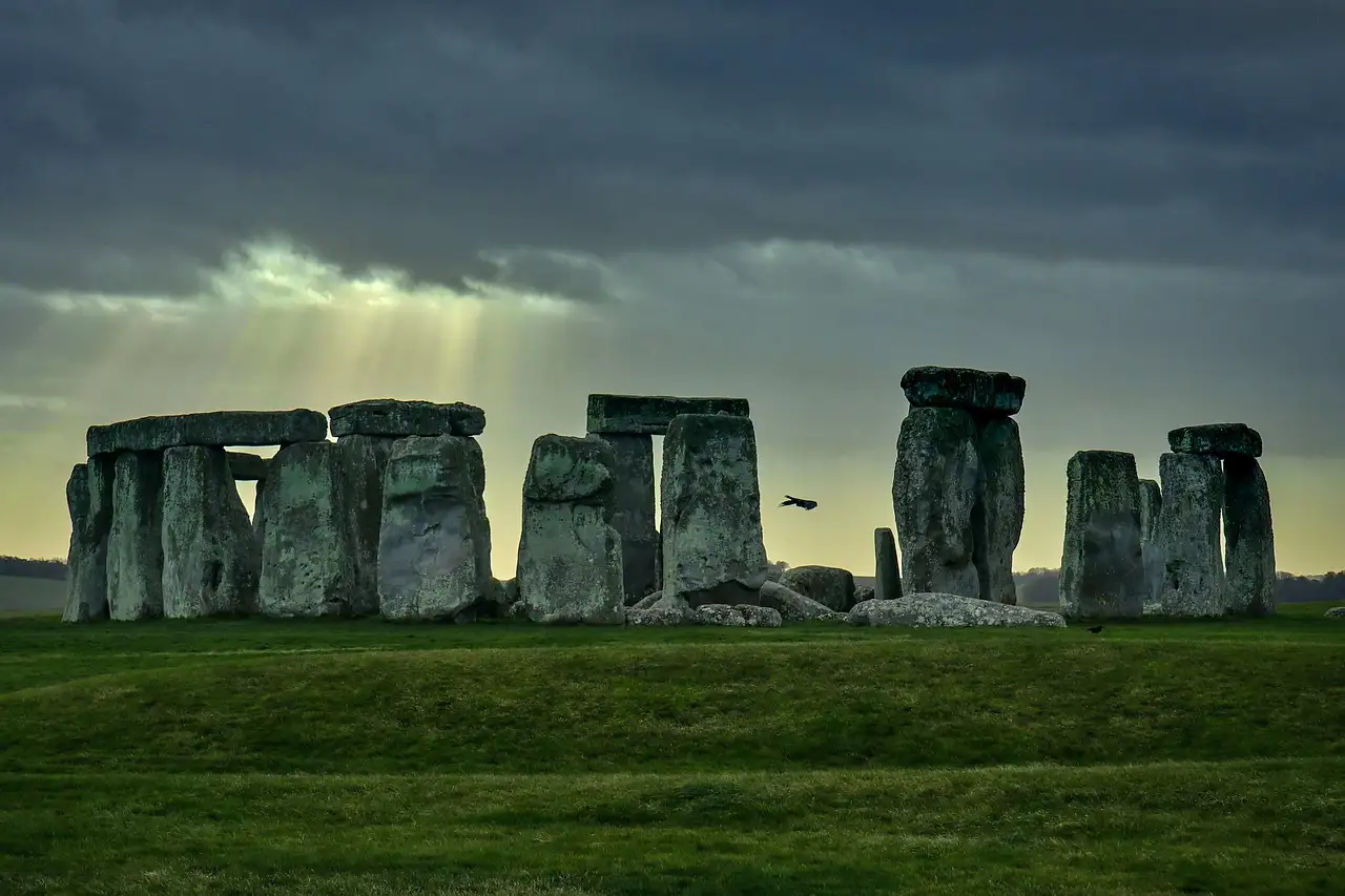 Stonehenge under a dark sky with sunbeams breaking through the clouds