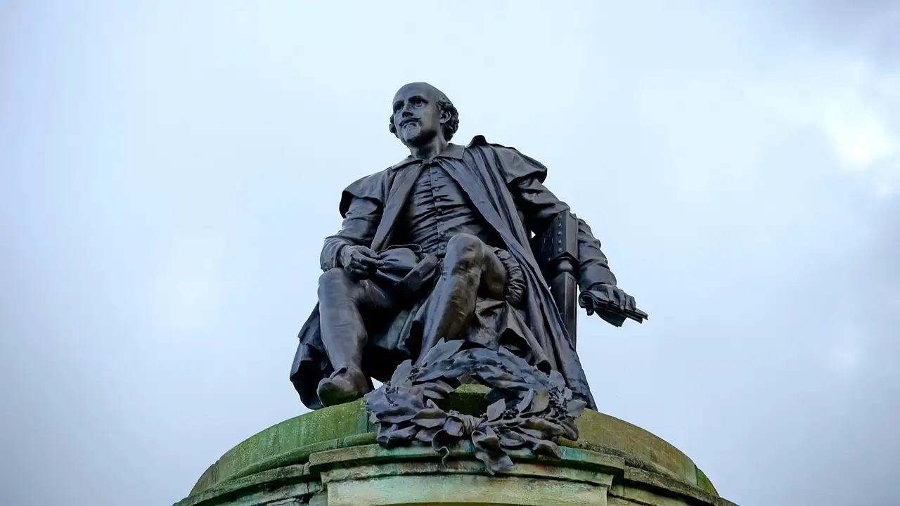 Bronze statue of a seated William Shakespeare against a cloudy sky