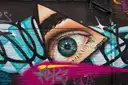 A large painted eye among graffiti tags on an East London wall