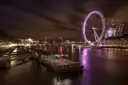The Thames at night with a lit pier and the London Eye glowing in the distance
