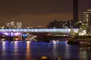 A bridge over the Thames lit up at night, with lights reflected on the river