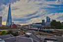 The glass spire of the Shard rising above London rooftops and railway lines under a cloudy blue sky