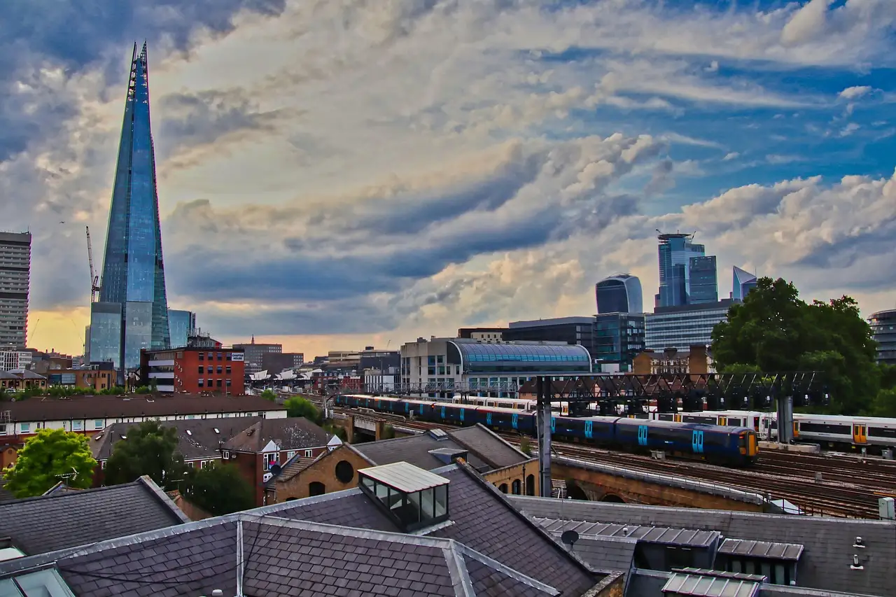 The glass spire of the Shard rising above London rooftops and railway lines under a cloudy blue sky