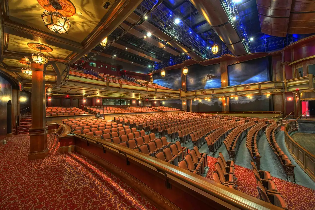 A grand theatre auditorium with tiers of seats under an ornate lit ceiling