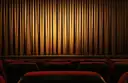A lit stage curtain behind rows of empty red theatre seats