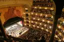 A packed theatre seen from the top balcony, with musicians playing on the stage below