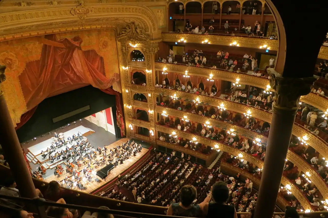 A packed theatre seen from the top balcony, with musicians playing on the stage below