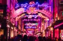 A crowded London street arched over with pink and blue neon Christmas lights