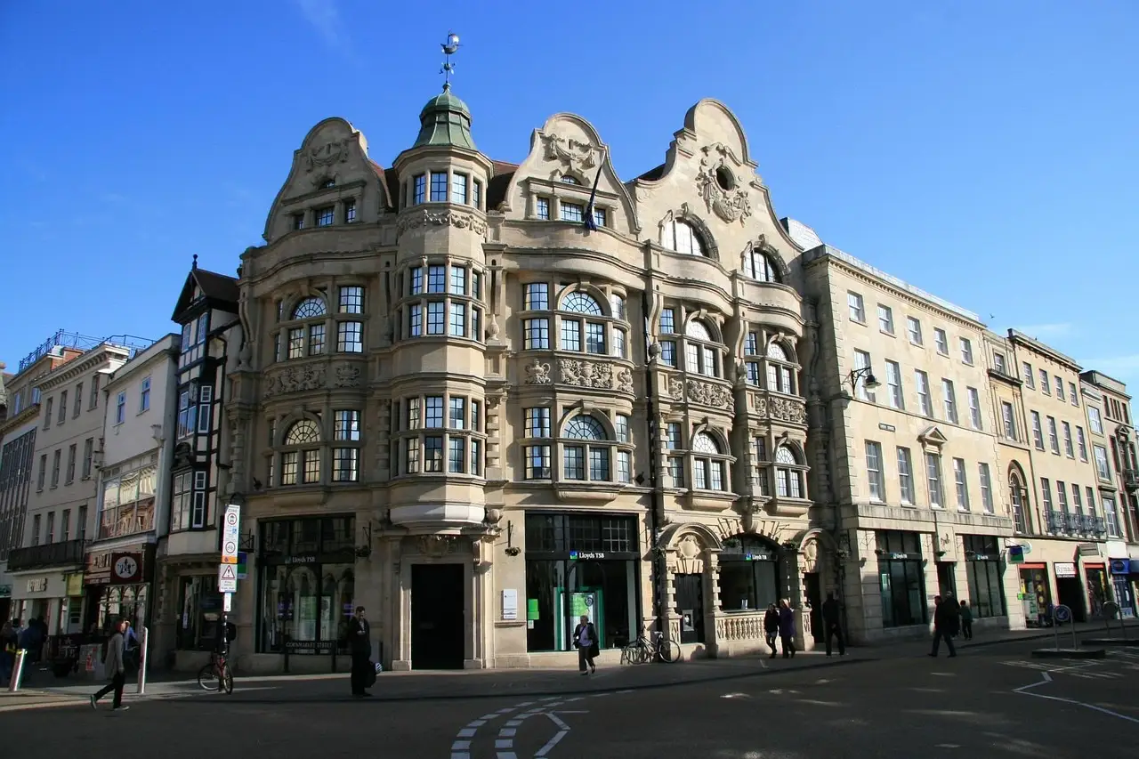 A grand stone corner building on a London shopping street under a blue sky