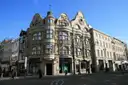 A grand stone corner building on a London shopping street under a blue sky