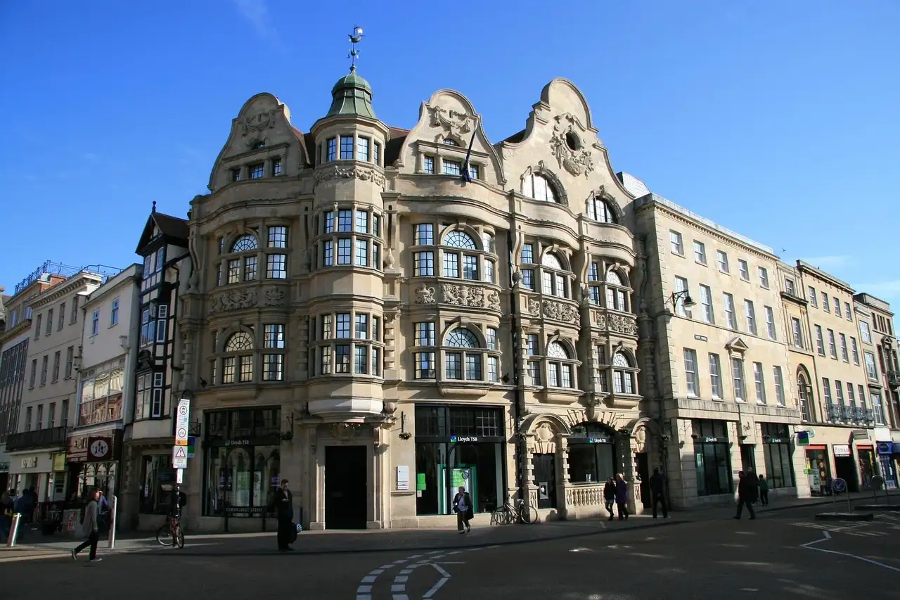 A grand stone corner building on a London shopping street under a blue sky