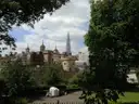 The walls of the Tower of London framed by trees, with the Shard in the distance