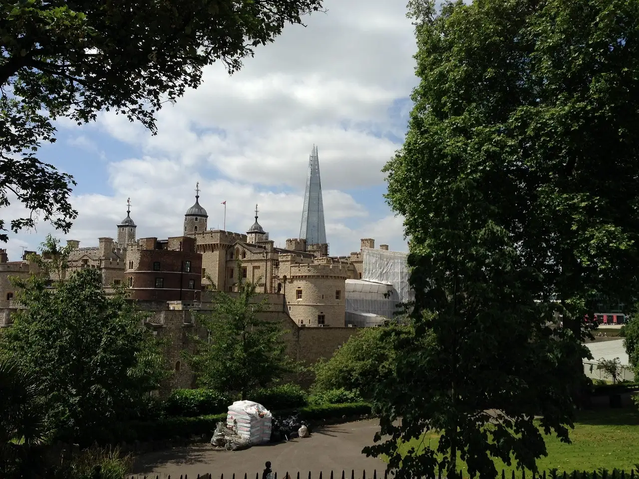 The walls of the Tower of London framed by trees, with the Shard in the distance