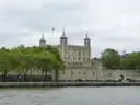 White Tower of the Tower of London above green trees, seen across the River Thames