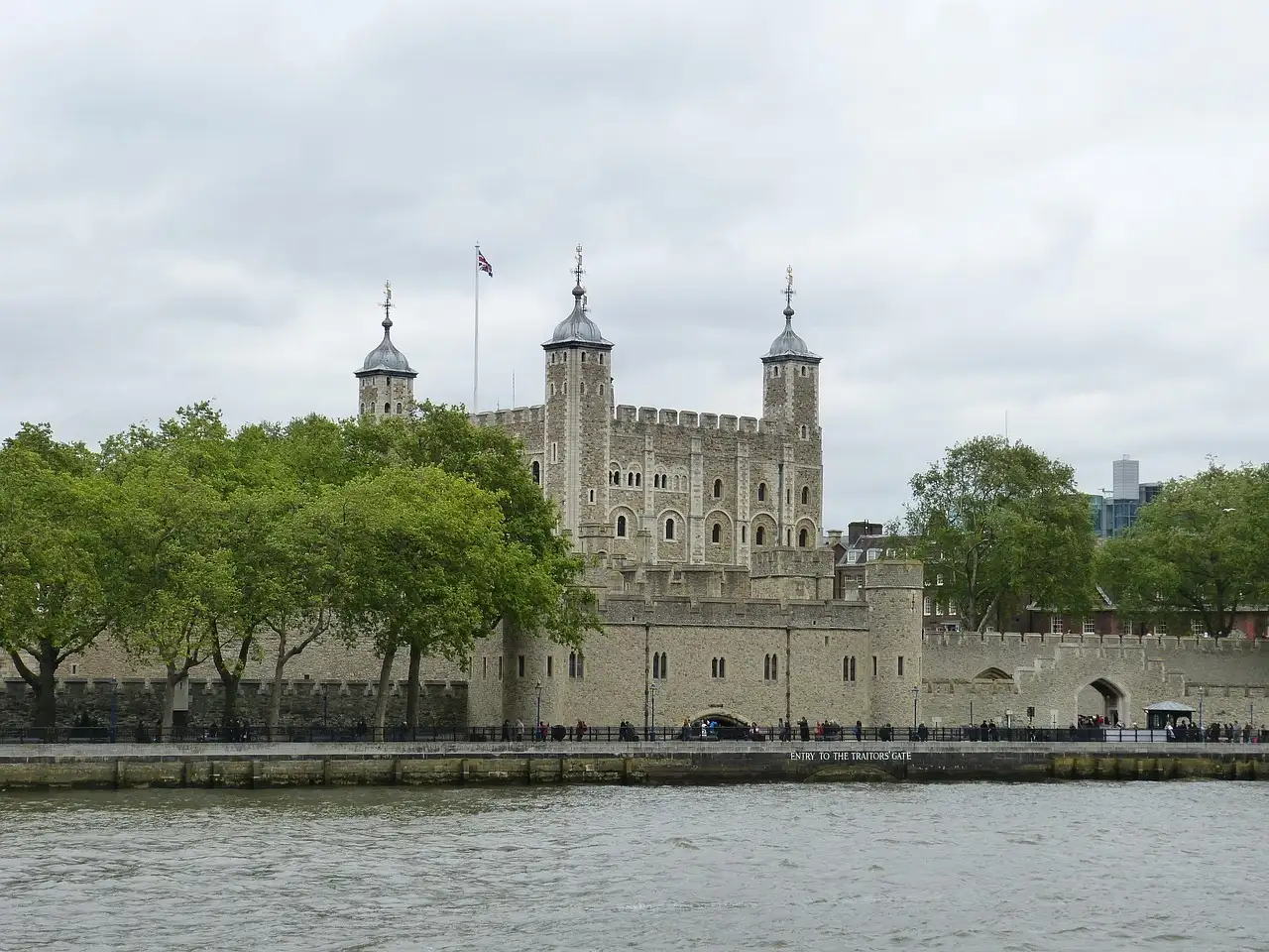 White Tower of the Tower of London above green trees, seen across the River Thames